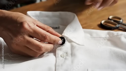Close-up of a person sewing a button onto a white shirt collar.