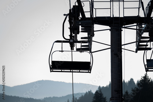 Chairlift elevated passenger ropeway. Empty chair lift bench. Ski station resort with chairlifts for skiers, snowboarders. Ski slope, piste, run or path down a mountain for snow skiing, snowboarding.