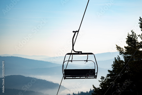 Chairlift elevated passenger ropeway. Empty chair lift bench. Ski station resort with chairlifts for skiers, snowboarders. Ski slope, piste, run or path down a mountain for snow skiing, snowboarding.