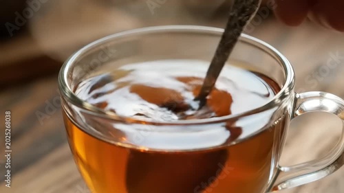 Close-up of a hand stirring tea in a clear glass cup.