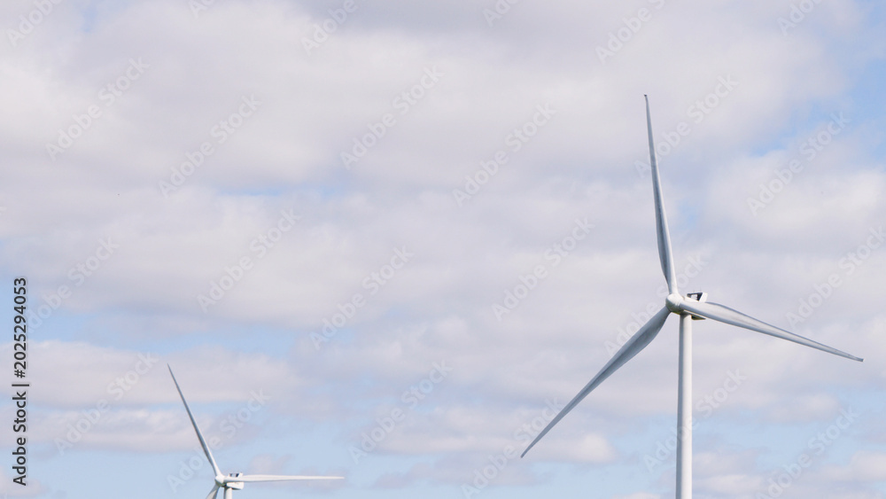 Fototapeta premium Large White Wind Turbines Against a Partly Cloudy Blue Sky