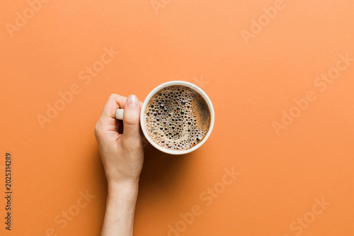 Minimalistic style woman hand holding a cup of coffee on Colored background. Flat lay, top view cappuccino cup. Empty place for text, copy space. Coffee addiction. Top view, flat lay