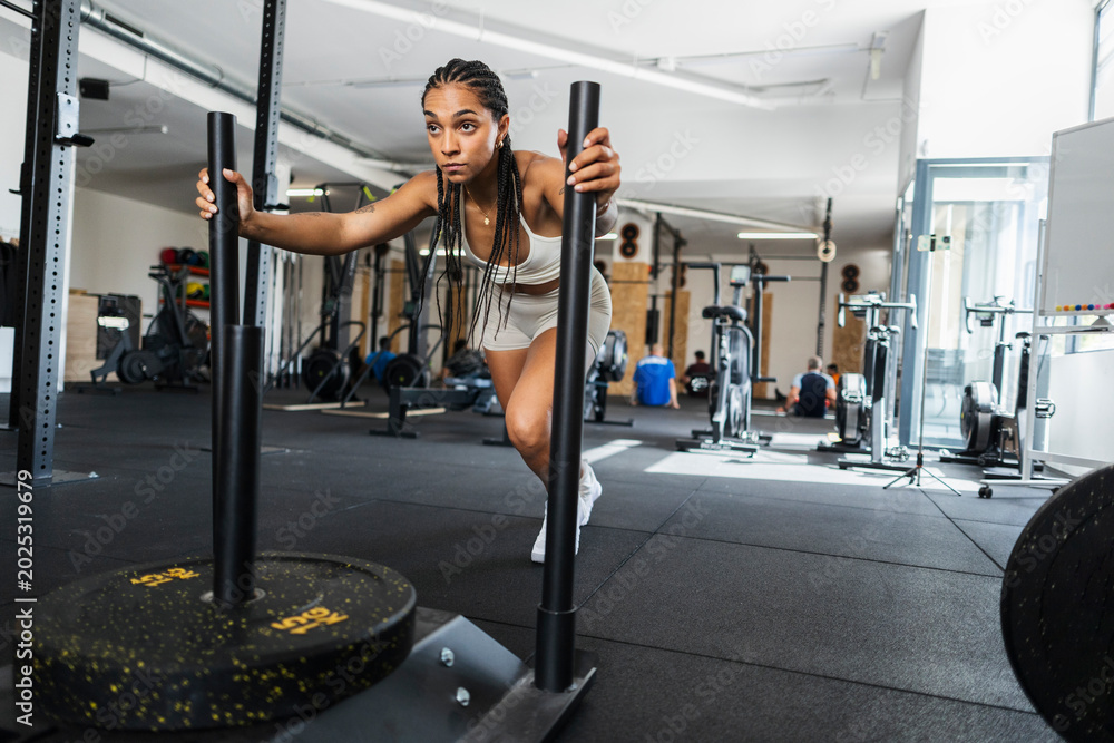 Fototapeta premium Determined woman pushing a heavy weight sled in a gym