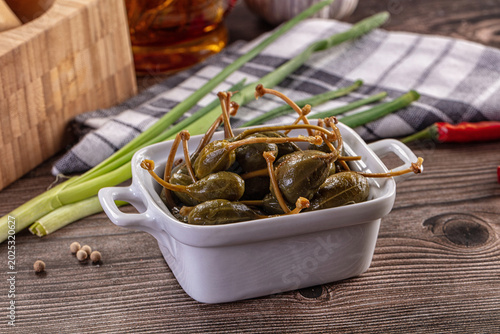 Foto Pickled caper berries in a bowl with fresh ingredients on a rustic wooden table