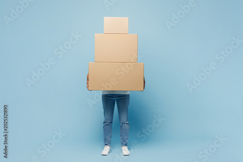 Full body delivery employee young woman wear white uniform workwear work as dealer courier hold in hand big stack cardboard box isolated on plain pastel light blue background studio. Service concept.