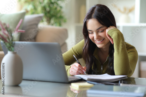 Happy young student taking notes studying at home