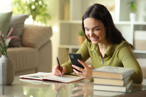 Happy young woman checking phone writing in agenda