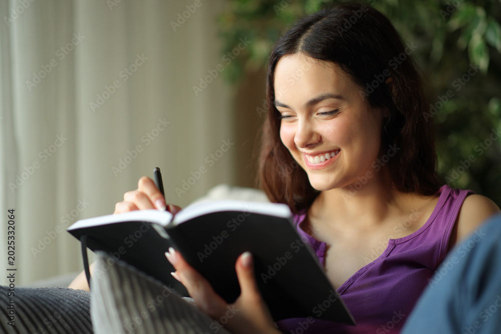 Fototapeta premium Happy young woman writing notes in paper agenda at home