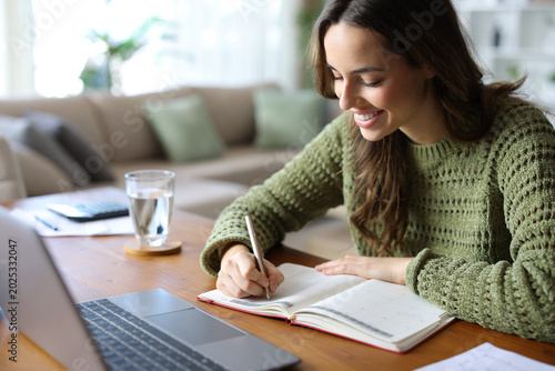 Happy teleworker writing in agenda working in a house