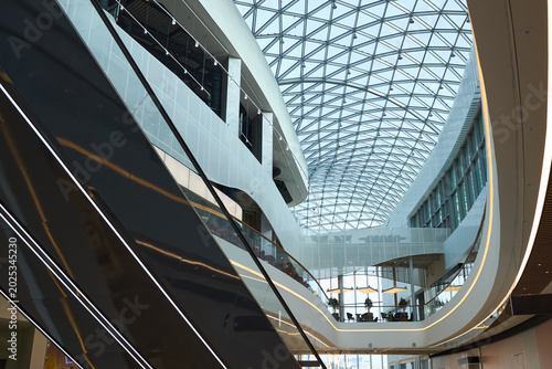 фотографія Wide angle view of modern commercial atrium featuring escalators, glass roof, cu