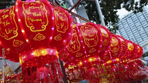 Traditional Vietnamese Tet holiday decoration close up. Red glowing lanterns with golden calligraphy text and lights at a festive street market during Lunar New Year in Nha Trang, Khanh Hoa, Vietnam.