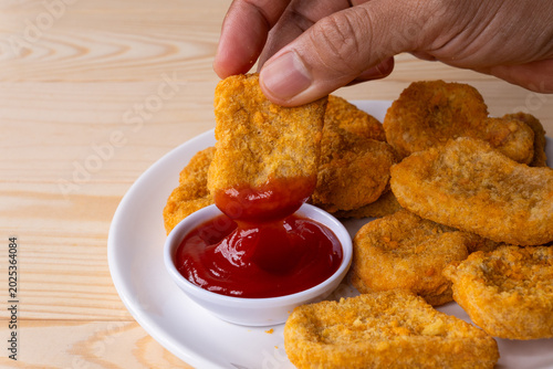 Obraz na plátne Hand dipping a crispy chicken nugget into a small bowl of ketchup