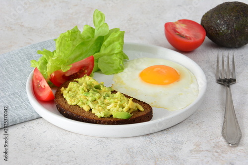 Healthy breakfast with fried egg, avocado toast, and fresh vegetables on a white plate
