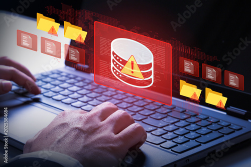 Cybersecurity Alert: A close-up shot of hands typing on a laptop keyboard with a red alert overlay displaying a database icon and warning symbols, signifying a cyber threat or data breach.