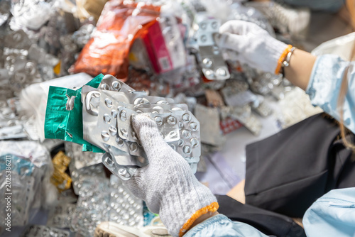 Gloved hand holding empty aluminum blister packs over a cardboard box for medical waste recycling and proper disposal.