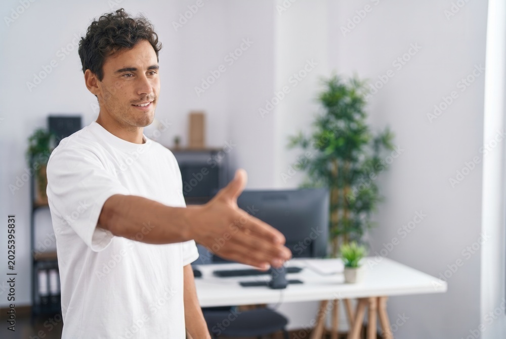 Fototapeta premium Young man extending his open hand forward, offering a handshake in a workspace