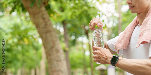 Asian man opening water bottle after outdoor fitness workout in park.