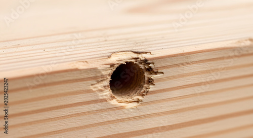 A close-up view of a hole drilled into a wooden plank with visible wood grain and texture.