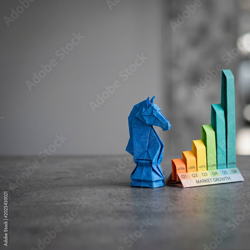 AI agent for business market growth concept with blue origami horse and rising bar chart on gray table