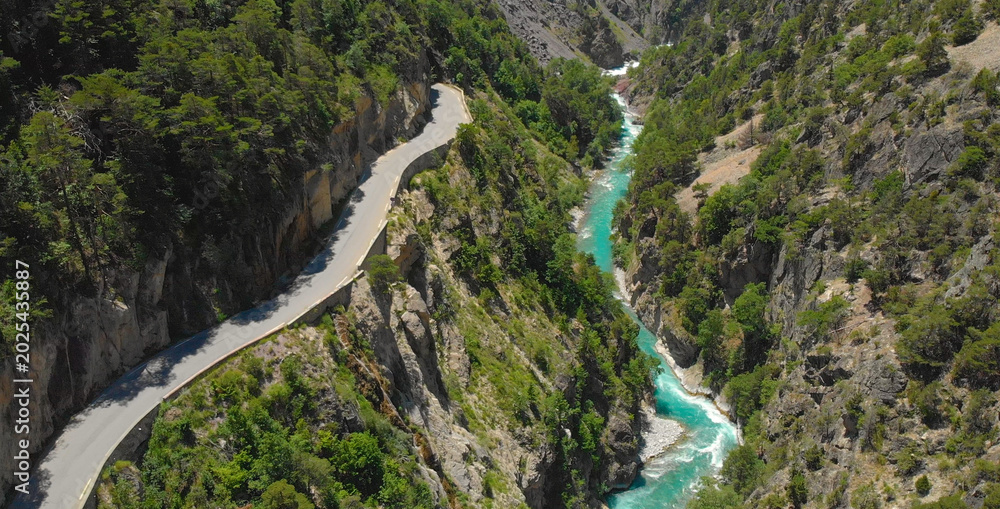 Fototapeta premium DRONE: Flying above an empty asphalt road leading into a tunnel above the river
