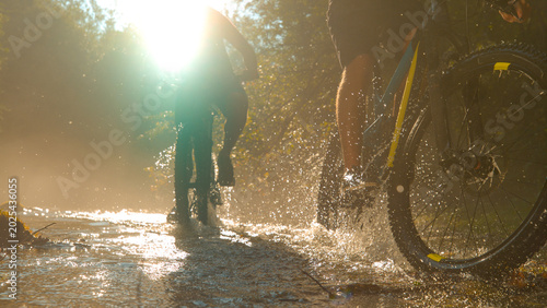 Bild auf Leinwand SUN FLARE: Blinding sunbeams illuminate the river as two men cycle across river