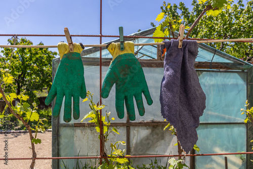 Garden gloves and cloth hanging on a wire fence.