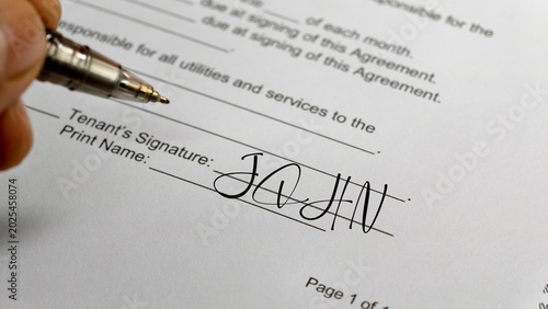 A close-up shot shows a hand holding a metallic ballpoint pen just after signing the name 