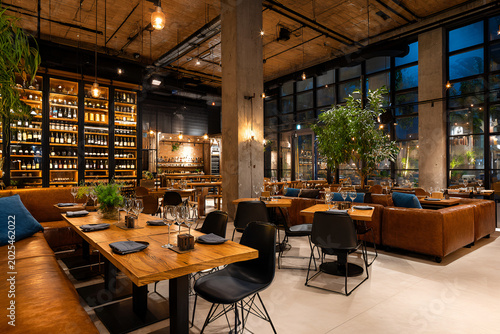 Modern dining area with wooden tables, leather seating, and large windows showcasing an outdoor evening view