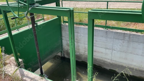 Water Gate Mechanism: A functional green metal water gate mechanism, controlling water flow in a channel, surrounded by lush vegetation and concrete structures.