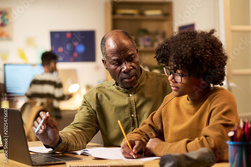 Foto Black senior man guiding Black teenager studying with laptop and notebook at home