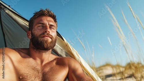 A serene image capturing a man enjoying his time at the beach inside a tent, basking in sunlight with a relaxed demeanor amidst soft grasses and clear skies.