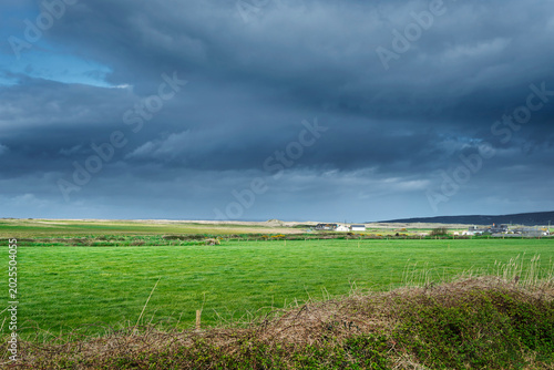 Atmospheric view of the Kerry countryside with sunlit fields and threatening storm clouds on the horizon.