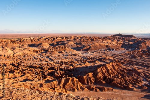 A vast eroded desert valley stretches across the Atacama Desert in northern Chile, illuminated by warm low sunlight
