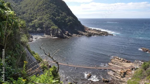 Authentic footage of a mother and daughter crossing a suspension bridge at Storm’s River Mouth in Tsitsikamma National Park captures togetherness and leisure against a scenic coastal backdrop.