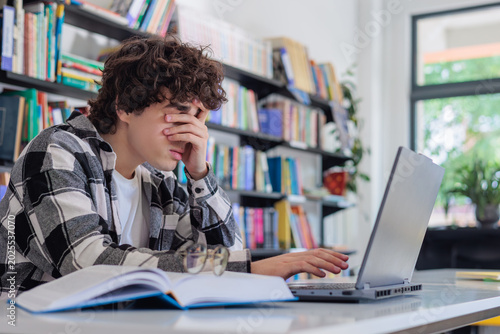 Obraz na plátně Stressed teenage student covering face while studying on laptop in library, academic pressure and mental overload