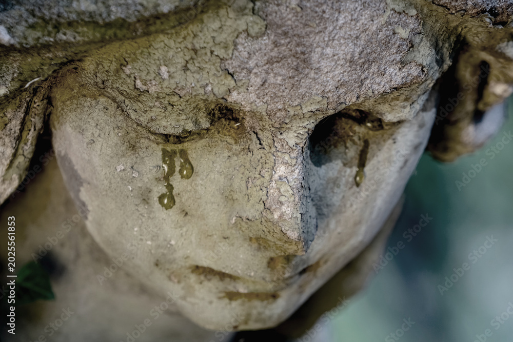 Fototapeta premium Close up of crying angel statue with weathered face and tear stains, symbolic image of sorrow, grief and eternal mourning