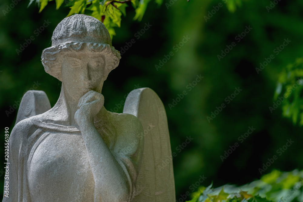 Fototapeta premium Thoughtful angel statue in peaceful green cemetery atmosphere