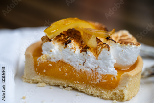 Bild auf Leinwand a sliced lemon meringue tartlet, revealing its crumbly buttery crust, vibrant yellow lemon curd filling, and fluffy toasted meringue topped with candied citrus peel
