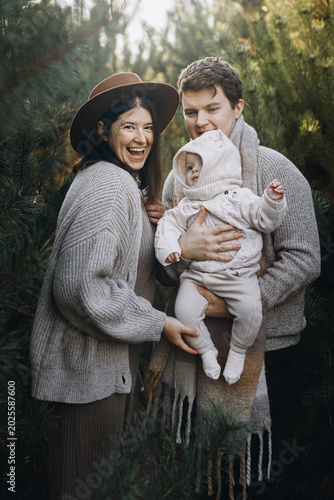 Happy family hugging with cute baby son in autumn woods in soft evening light. Parenthood. Mother father and little child in cozy stylish clothes smiling in fall park