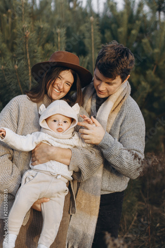 Happy family having fun with cute baby son in autumn woods in soft evening light. Parenthood. Mother father and little child in cozy stylish clothes smiling in fall park