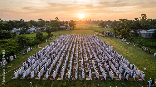 Large group of muslim men performing congregational prayer in an open green field during sunrise or sunset with congregation religion community gathering landscape spiritual peaceful devotion