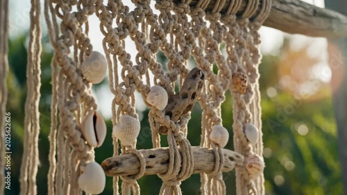 Close-up of a decorative macrame wall hanging with seashells and driftwood hanging outdoors in natural sunlight