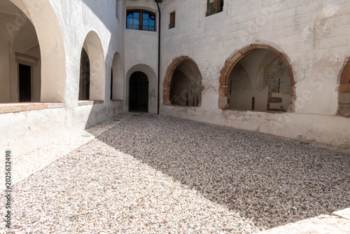Foto An open-air view of a historic monastery courtyard featuring cobblestone ground, white plastered walls, and medieval stone archways under bright daylight