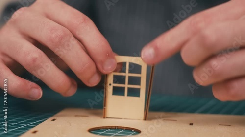 Installing wooden front door in miniature house model kit. DIY home construction featuring architecture craft creativity and plywood assembly on cutting mat. New housing concept with real estate