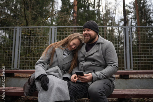 Картината върху платно Happy couple sharing a moment outdoors, the man holding a smartphone with earpho