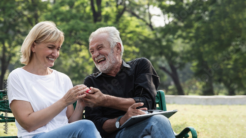 Elder healthy sits on green bench in vibrant park, enjoying moment of leisure. individual holds red object while using tablet, surrounded by lush greenery. This evokes sense of calm and connection