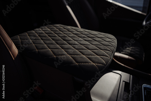 Close-up of a premium car central armrest upholstered in quilted black alcantara fabric with contrast stitching.