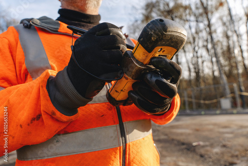 Tableau sur toile Worker uses drill at construction site during late afternoon with trees in backg