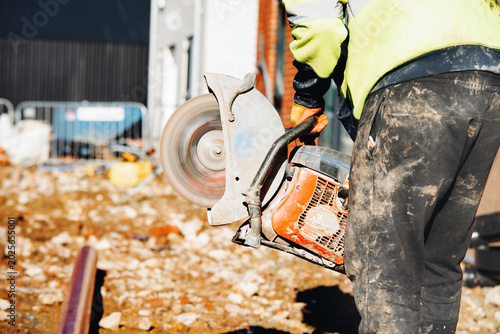 Canvas Print Construction worker cuts stone with saw at building site in afternoon sun with d