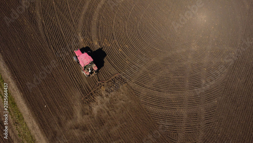 Fotografie Aerial View of a Red Tractor Harrowing a Large Agricultural Field